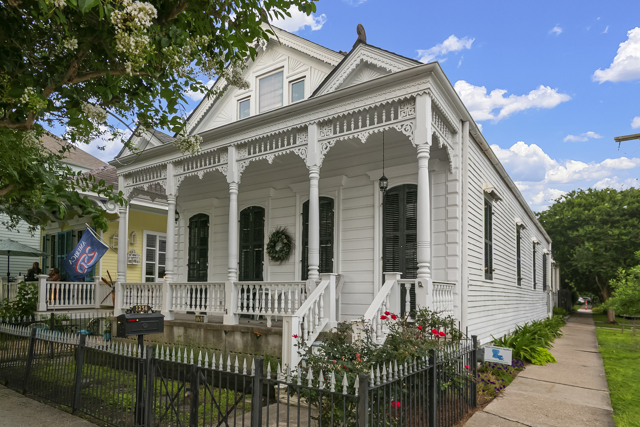 White Victorian shotgun house with gingerbread trim and a wide front porch in Mid-City, New Orleans